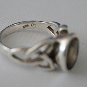 May include: Silver ring with a Celtic knot design and a black stone. The ring is marked with a 'C' inside a circle.