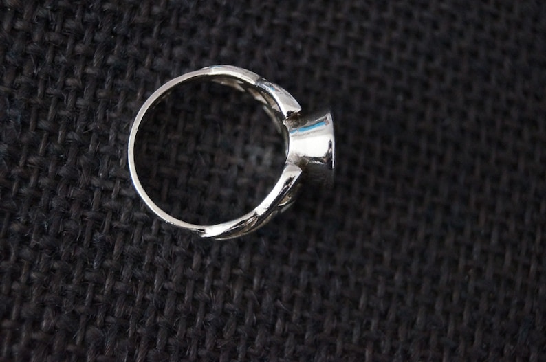 May include: A silver ring with a round, faceted gemstone. The ring has a delicate, intricate design.