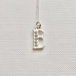 May include: A silver necklace with a pendant in the shape of the letter E. The letter is adorned with clear rhinestones.