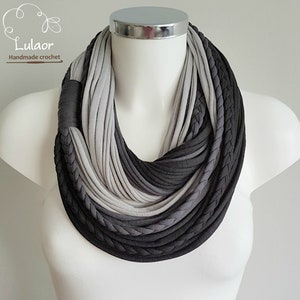 May include: A gray and black infinity scarf made of crocheted fabric. The scarf is layered and has a braided design.