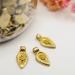 Peut inclure: Trois breloques en forme de feuille dorées avec un motif texturé. Les breloques ont une boucle en haut pour être attachées à des bijoux ou d'autres objets artisanaux.