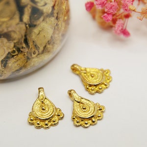 Puede incluir: Tres abalorios de metal de color dorado en forma de lágrima con un diseño circular y un borde de cuentas.