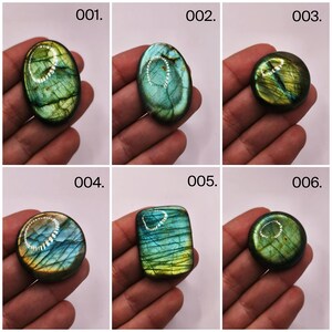 May include: Six polished labradorite gemstones in various shapes: oval, round, and rectangular. The stones display iridescent flashes of blue, green, and yellow. Each stone is held in a hand, with the numbers 001 through 006 visible.