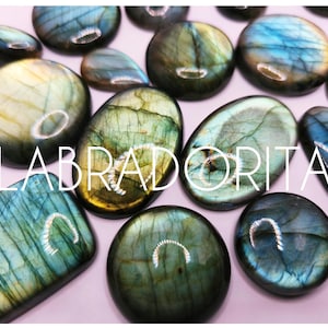 May include: A collection of polished labradorite gemstones in various shapes, including oval, round, and rectangular. The stones display iridescent colors of blue, green, and gold. The word "LABRADORITA" is written across the image.