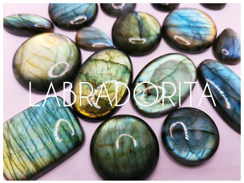 May include: A collection of polished labradorite gemstones in various shapes, including oval, round, and rectangular. The stones display iridescent colors of blue, green, and gold. The word "LABRADORITA" is written across the image.