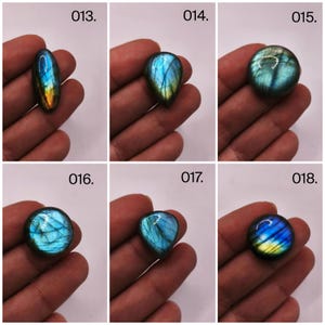 May include: Six polished labradorite gemstones in various shapes: oval, teardrop, and round. Each stone displays a vibrant play of color, with blues, greens, and yellows shimmering across their surfaces. The gemstones are held in a hand, showcasing their natural beauty.