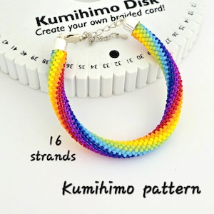 Puede incluir: Una pulsera Kumihimo de colores arcoíris con 16 hebras, exhibida en un disco Kumihimo blanco. La pulsera presenta un degradado de colores, incluyendo rojo, naranja, amarillo, verde, azul y morado. El texto "Kumihimo pattern" es visible.