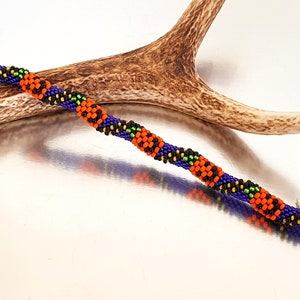 May include: A beaded bracelet with a repeating pattern of orange, black, green, and purple beads. The bracelet has silver clasps on each end.