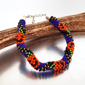 May include: A beaded bracelet with a spiral design in black, orange, green, and purple beads. The bracelet has a silver clasp.