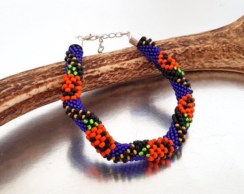 May include: A beaded bracelet with a spiral design in black, orange, green, and purple beads. The bracelet has a silver clasp.