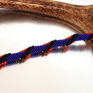 May include: A beaded bracelet with a spiral pattern in shades of purple, black, orange, and gold.