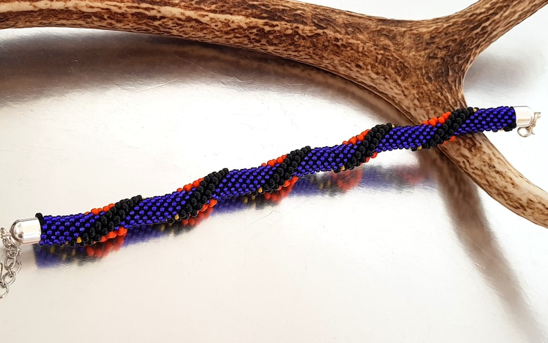 May include: A beaded bracelet with a spiral pattern in shades of purple, black, orange, and gold.