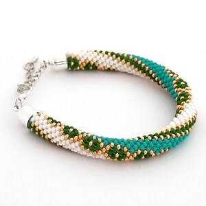 May include: A white, green, and gold beaded bracelet with a silver clasp.