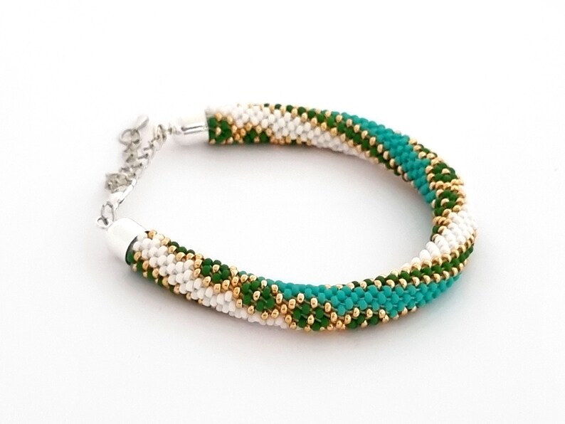 May include: A white, green, and gold beaded bracelet with a silver clasp.