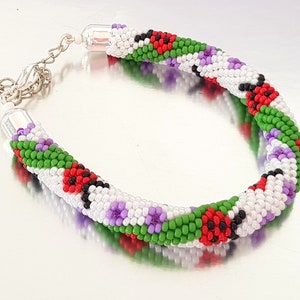 May include: A beaded bracelet with a spiral design. The bracelet features white, green, red, black, and purple beads. The bracelet has a silver-colored clasp and end caps.