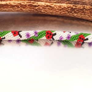 May include: A beaded bracelet with a spiral design. The bracelet features white, red, green, and purple beads. The bracelet has silver-colored clasps on each end. The bracelet is approximately 7 inches long.