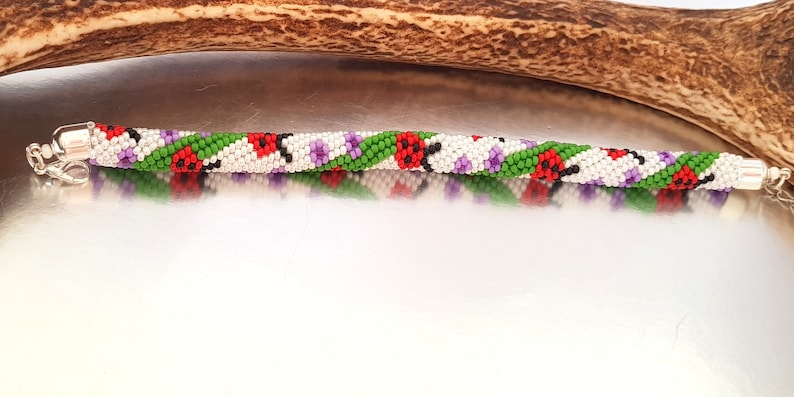 May include: A beaded bracelet with a spiral design. The bracelet features white, red, green, and purple beads. The bracelet has silver-colored clasps on each end. The bracelet is approximately 7 inches long.