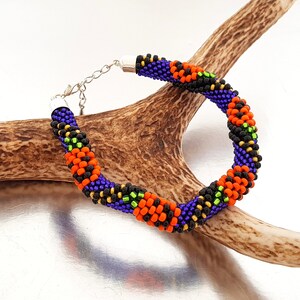 May include: A beaded bracelet with a repeating pattern of orange, black, green, and purple beads. The bracelet is on a brown antler.