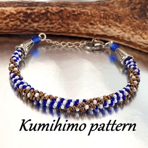 Peut inclure: Un bracelet en perles bleu, blanc et marron avec des fermoirs argentés. Le bracelet est réalisé à l'aide de la technique du kumihimo, une méthode de tressage traditionnelle japonaise. "Kumihimo pattern" est écrit sous le bracelet.