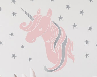 May include: A pink unicorn head silhouette with a silver horn and mane, against a white wall with silver star decals. A white crib with a pink blanket and pillows is in the foreground.
