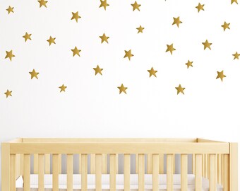 May include: A white crib with a wooden frame and gold star decals on the wall behind it.