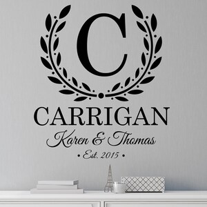 Könnte beinhalten: Schwarzer und weißer Wandaufkleber mit einem Lorbeerkranz-Design, das den Buchstaben C umgibt. Der Text "CARRIGAN Karen & Thomas Est. 2015" befindet sich unterhalb des Kranzes.