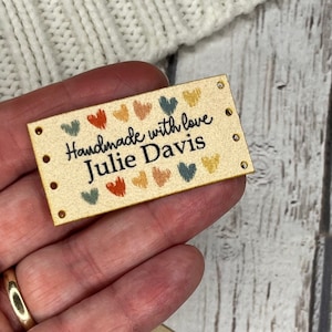 May include: A brown leather label with the text "Handmade with love Julie Davis" and colorful hearts printed on it. The label has holes punched around the edges.