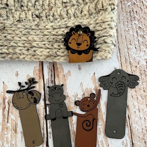 May include: Five colourful leather bookmarks with animal illustrations. The bookmarks feature a sloth, a hippopotamus, a monkey, an elephant, and a lion. The bookmarks are all rectangular and have a hole at the top for hanging.