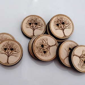 May include: A set of 10 wooden buttons with a laser-etched tree design. The buttons are light brown with a dark brown tree design. Each button has two holes.