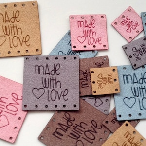 May include: Assortment of small square fabric tags with the text "Made with Love" in various colours, including brown, pink, grey, and blue.
