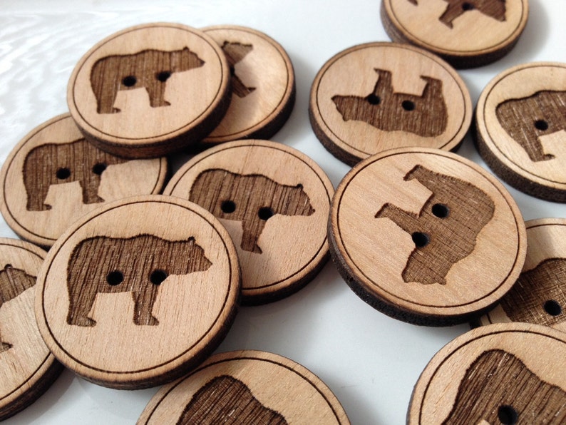 May include: A collection of wooden buttons with a bear design. The buttons are round and have a natural wood finish. Each button features a different bear silhouette.