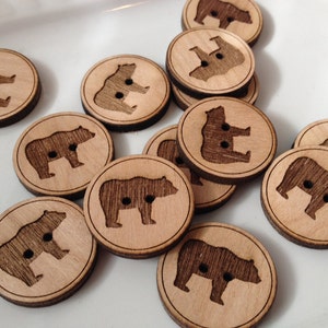 May include: A collection of wooden buttons featuring a bear silhouette design. The buttons are round and have a natural wood finish.