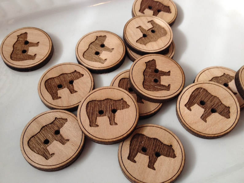 May include: A collection of wooden buttons featuring a bear silhouette design. The buttons are round and have a natural wood finish.