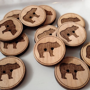 May include: A collection of wooden buttons with a bear silhouette design. The buttons are light brown and have a natural wood finish.