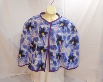 May include: A purple fleece cape with a floral print of blue pansies. The cape has a purple trim and a center seam.