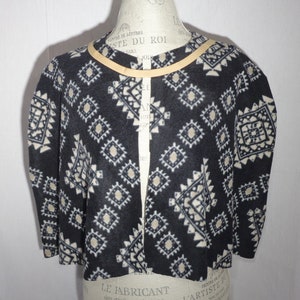 May include: Black and white geometric patterned fleece cardigan with a tan trim around the neckline.