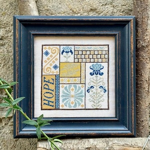 May include: A framed cross-stitch artwork with a navy blue frame. The artwork features a geometric design with the word "HOPE" vertically stitched in yellow. The design incorporates yellow, blue, and white floral and geometric patterns. The artwork is displayed against a neutral background.