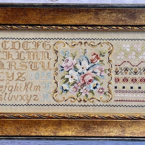 May include: A framed cross-stitch sampler with a floral design, alphabet, and decorative borders. The sampler is in a gold frame with a rope-like design.