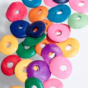 May include: A collection of colorful wooden donut-shaped beads with holes in the center. The beads are in various colors, including pink, blue, green, yellow, orange, red, and purple.