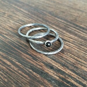 May include: Three silver rings stacked on a wooden surface. The top ring has a black gemstone.