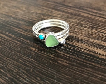 Puede incluir: Un anillo de plata con tres bandas, un triángulo de vidrio de mar verde y una piedra turquesa.