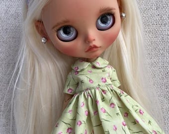 Puede incluir: Una muñeca con el pelo largo y rubio que lleva un vestido verde claro con flores rosas y una diadema rosa.