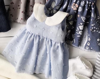 May include: A light blue dress with a white collar and a dotted pattern. The dress is made of a soft, textured fabric and has a ruffled hem.
