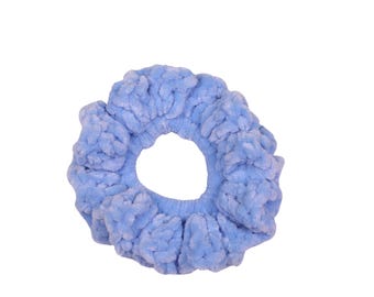May include: A light blue scrunchie made of a soft, plush material. The hair accessory is round with a hole in the center and is designed to hold hair in a ponytail or bun. The scrunchie is a solid color and has a textured appearance.