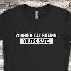 Könnte beinhalten: Schwarzes T-Shirt mit weißem Text, der "Zombies Eat Brains. You're Safe." lautet.