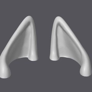 May include: A pair of white, sculpted, pointed ears. The ears are curved and have a smooth, rounded surface.