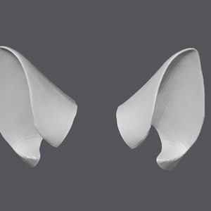 Puede incluir: Dos formas blancas abstractas con forma de oreja se muestran sobre un fondo gris. Las formas tienen un diseño curvo y plegado, con un aspecto texturizado. Las formas son simétricas y parecen estar renderizadas en 3D.