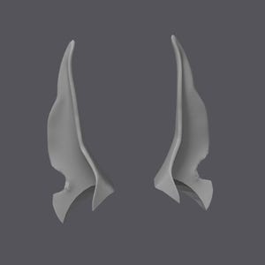 May include: A pair of grey, pointed elf ear prosthetics. The ears are curved and have a textured surface, with a small notch on the lower edge. The background is a solid grey.