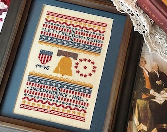May include: A framed cross-stitch sampler with a patriotic theme. The sampler features a bell, stars, and the text "Let Freedom Ring" and "Independence Hall 1776".