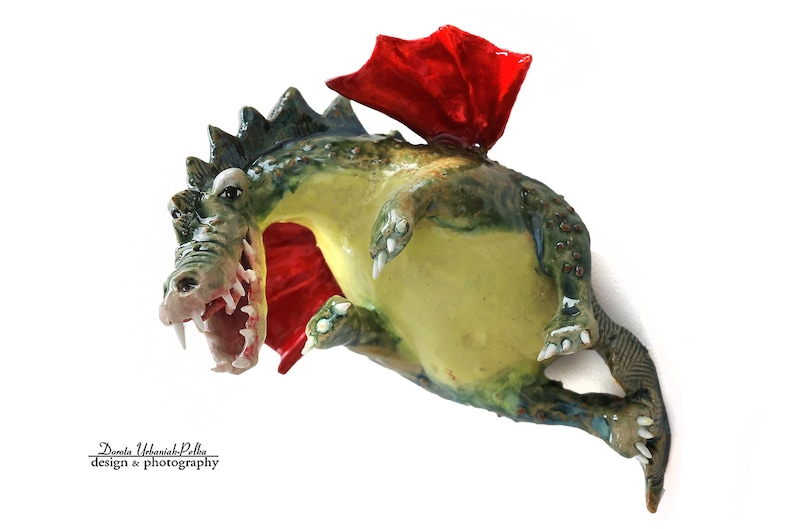 Pu&ograve; includere: Figurina di drago artigianale con corpo verde e giallo, ali rosse e bocca aperta. Il drago &egrave; raffigurato in volo, con una superficie strutturata e dettagliata. Design stravagante.